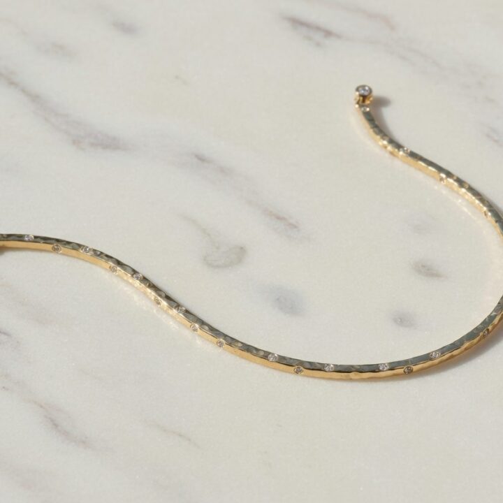 A hammered gold bracelet set with small diamonds, photographed on pale marble.