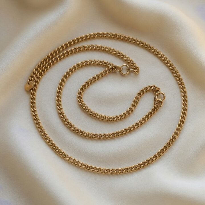 Two gold curb chains, one longer and one shorter, photographed on ivory silk.