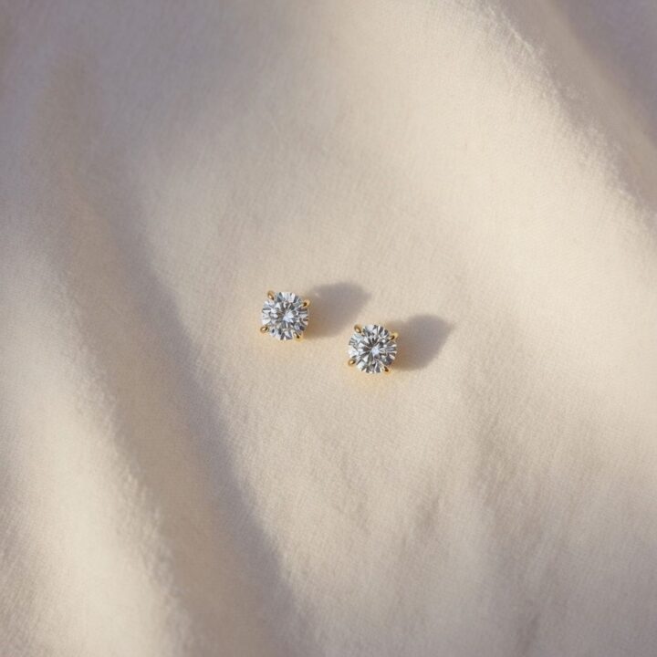 A pair of round diamond studs, photographed on cream linen.